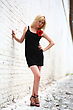 Beautiful Young Girl In Black Dress With Red Flower Against A Brick Wall